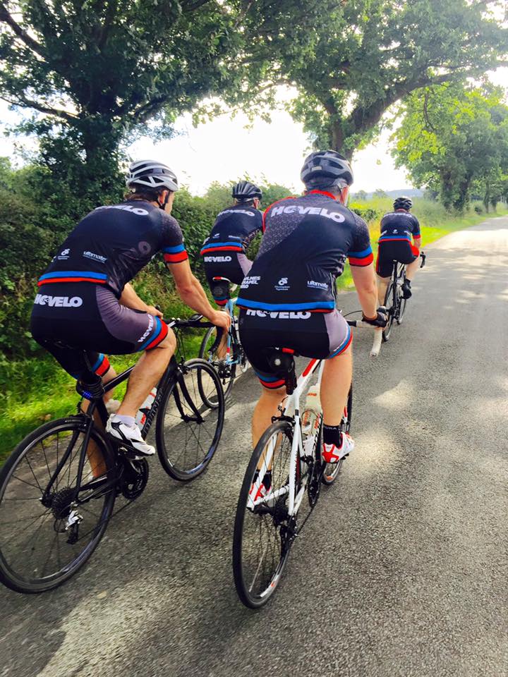 4 cyclists in hc-velo jerseys riding down a country lane